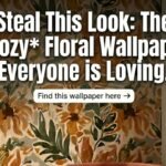 Cozy reading nook featuring a rust orange velvet armchair with a chunky knit blanket, set against a trending floral wallpaper accent wall in earthy mustard and green tones. Rustic wooden side table with coffee and books. Text overlay reads: Steal This Look.